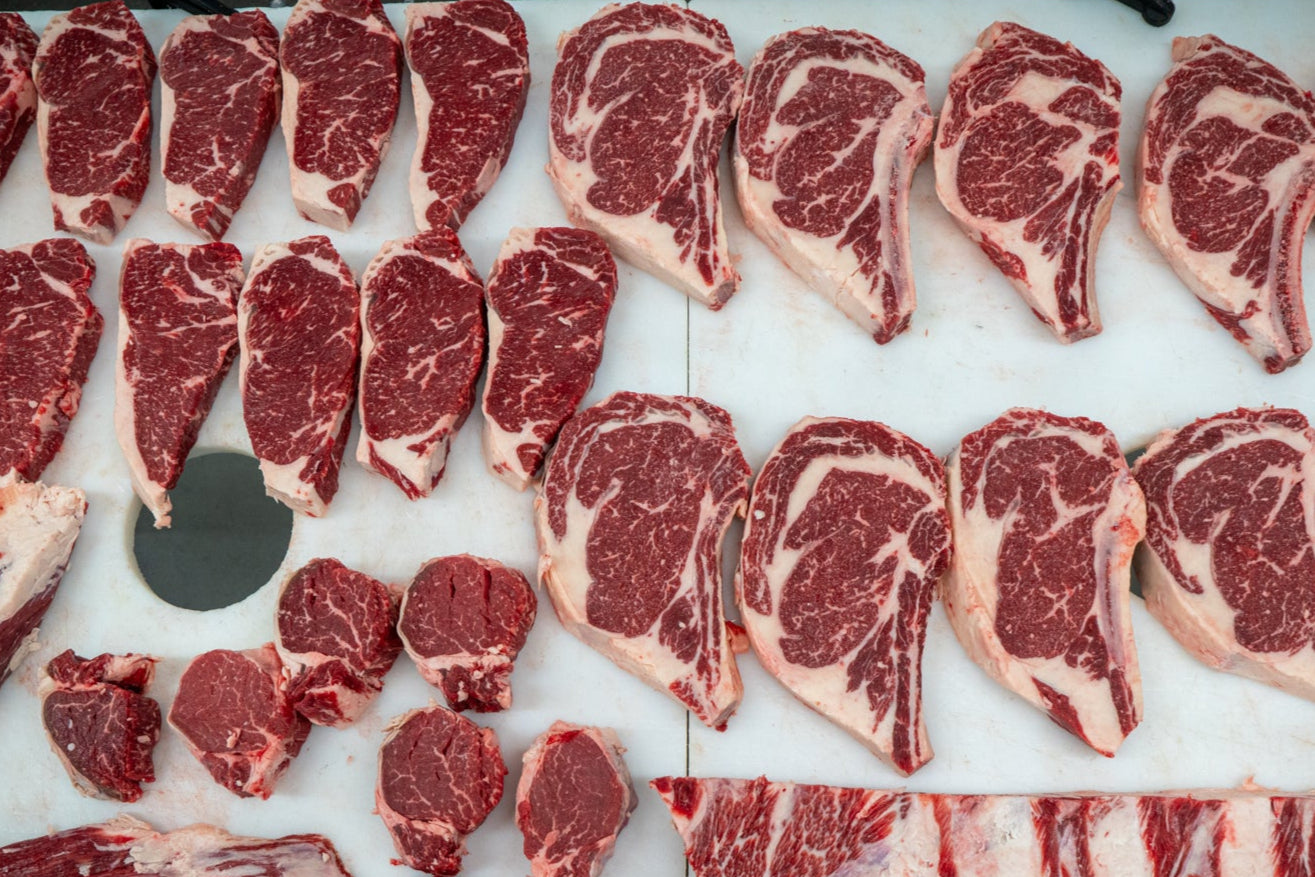 Assorted cuts of raw red meat on a white cutting board.